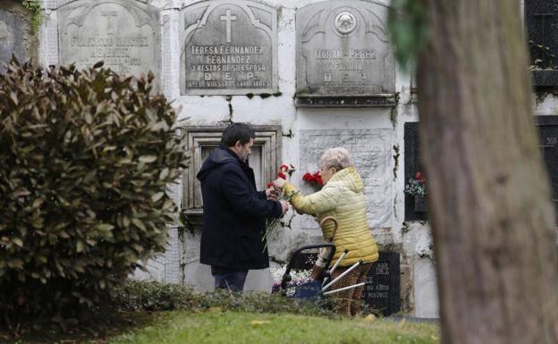 Dos personas depositan flores en un nicho en el cementerio de Ceares.