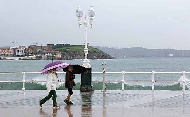 Dos mujeres pasean bajo la lluvia por el Muro.