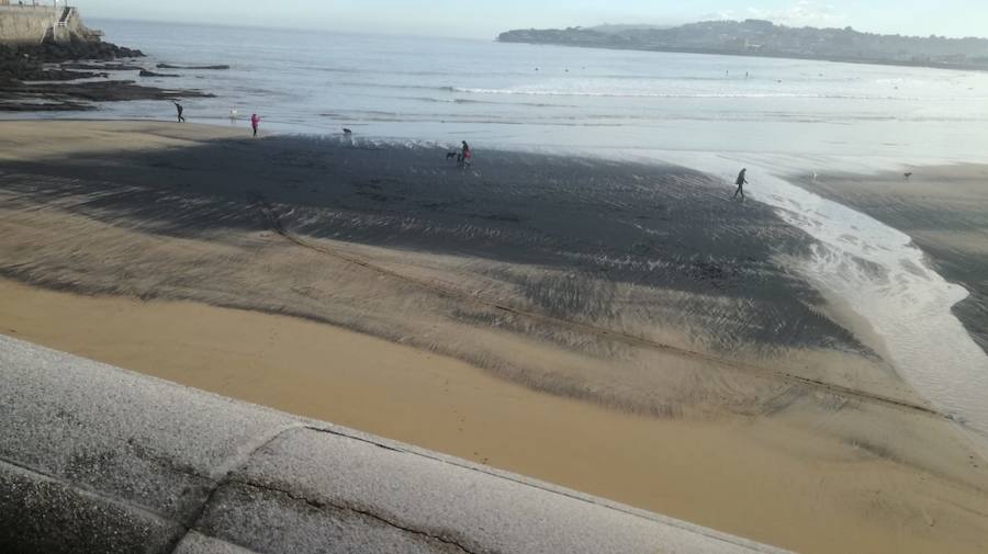 La playa de San Lorenzo de Gijón ha amanecido cubierta por una nueva mancha de carbón. A pesar de que no es una situación desconocida para los vecinos, muchos no han dudado en inmortalizar la estampa.
