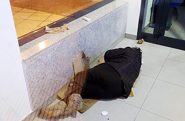 Una mujer duerme en el interior de un cajero sin más abrigo que su ropa y unos cartones. 