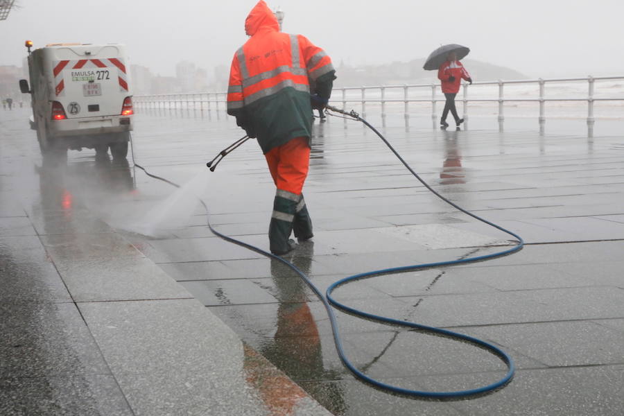 El paseo gijonés del Muro ha amanecido con algunas de sus escaleras cerradas debido a los daños causados por el temporal de lluvia y viento. Operarios de Emulsa han procedido a la limpieza de la arena depositada en el paseo tras la pleamar.