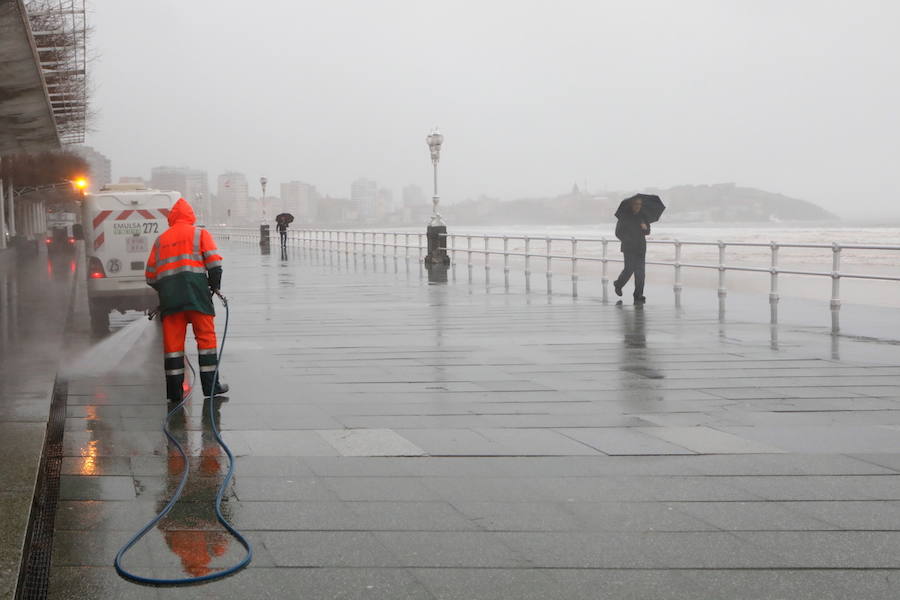 El paseo gijonés del Muro ha amanecido con algunas de sus escaleras cerradas debido a los daños causados por el temporal de lluvia y viento. Operarios de Emulsa han procedido a la limpieza de la arena depositada en el paseo tras la pleamar.