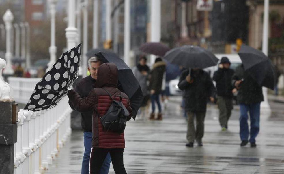 Varias personas tratan de protegerse del viento y la lluvia en Gijón.