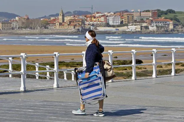 Una mujer se dirige a la playa de San Lorenzo para disfrutar de la jornada de sol y calor.