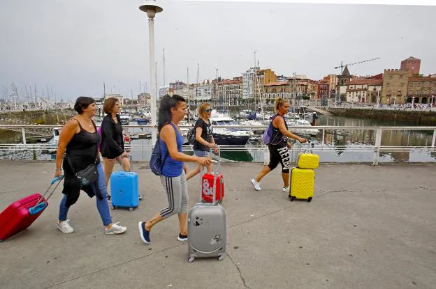 Un grupo de turistas camina con sus respectivas maletas por el puerto deportivo. 