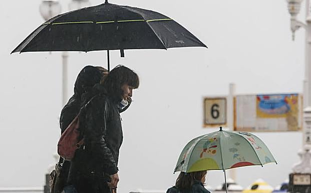 Varias personas pasean bajo la lluvia por Gijón.