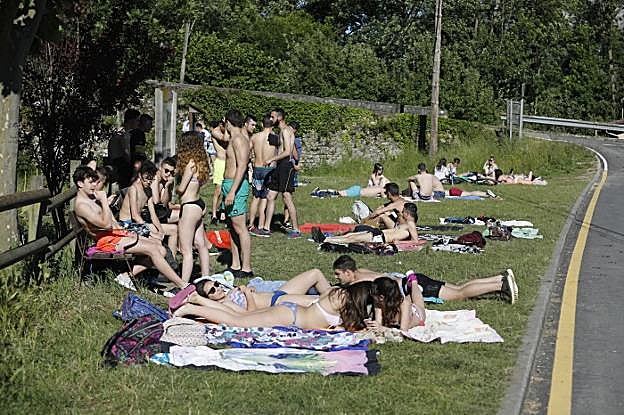 Laviana. Varios jóvenes toman el sol sin importar la cercanía de la carretera. 
