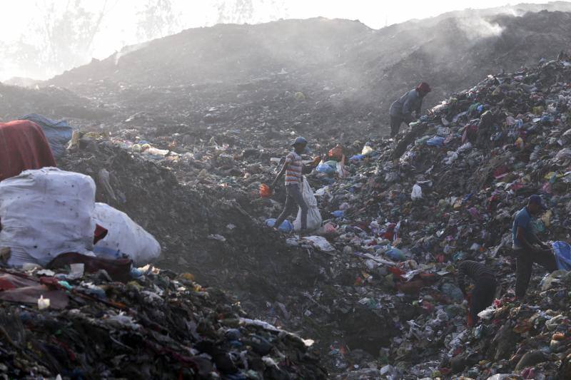 Los carroñeros de la India recogen material utilizable entre la basura, mientras el humo sale de un incendio en un depósito contiguo a la ciudad de Amritsar