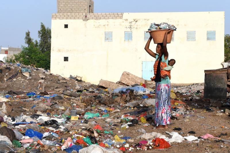 Una mujer con su bebé lleva una palangana llena de desechos a un área de recolección de basura en Rufisque, cerca de Dakar. 