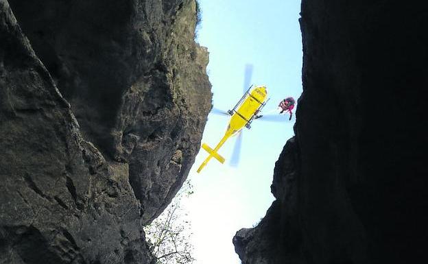 Los bomberos izan al herido hasta el helicóptero. 