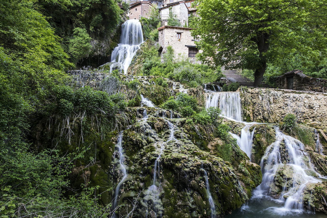 Orbaneja del Castillo (Burgos): Si por algo destaca este pueblo burgalés es por el la magia de su paisaje modelado por el agua. Del municipio, declarado Conjunto Histórico, destacan sus estrechas calles medievales, las pozas y las casas de cuento, todo con Cañón del río Ebro de fondo. No obstante, si existe una imagen idílica de este paraje es la que genera la Cueva del Agua y es, además, la primera con la que te vas a encontrar al visitar el pueblo: casas atravesadas por las aguas del arroyo, que cae en forma de escalera de unos 25 metros de altura, formando una casacada.