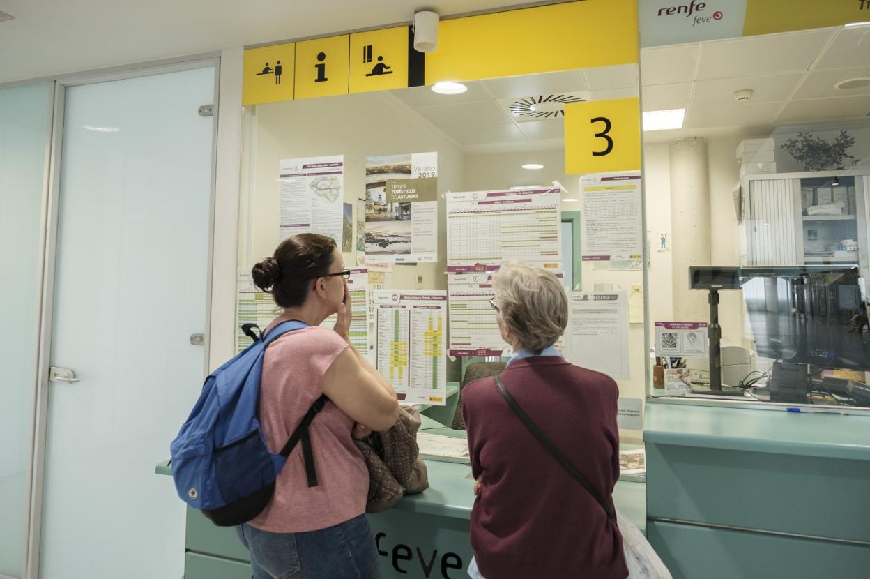 Dos viajeras consultan los horarios de Feve en la estación de Gijón. 