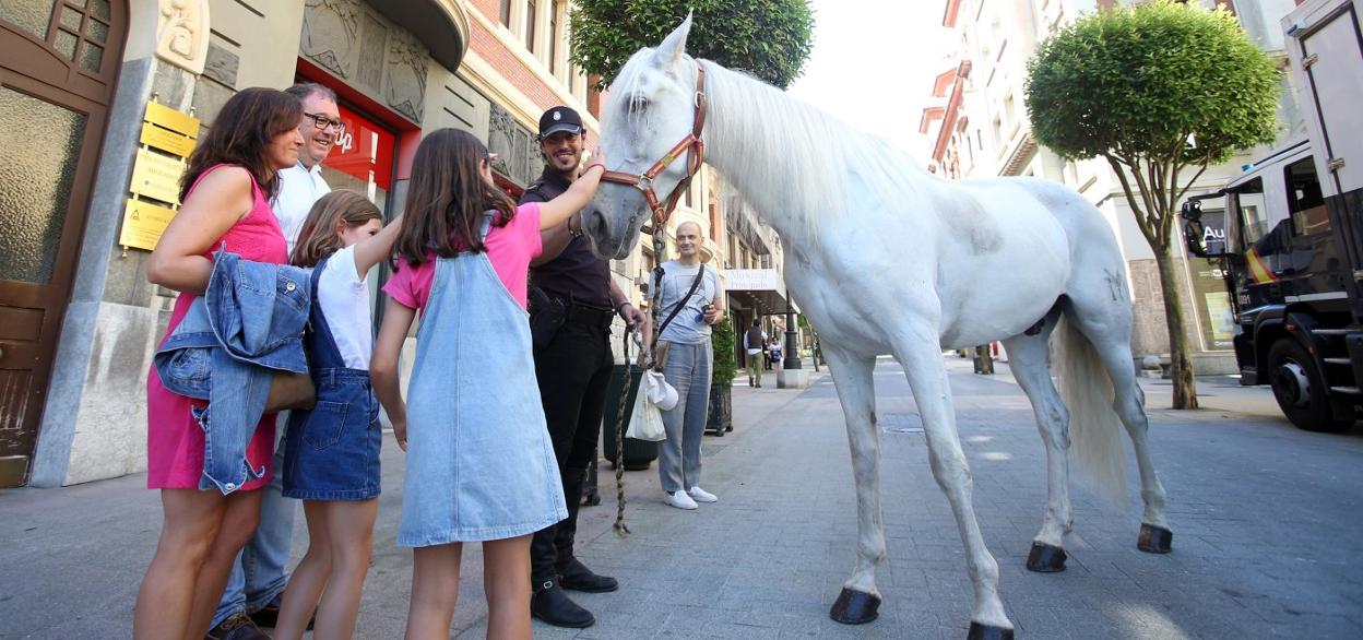 Dos niñas acarician uno de los caballos en presencia del agente de la Policía Nacional en la calle Principado. 