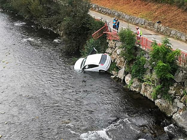 Tres ciclistas observan el vehículo siniestrado en las aguas del río Nalón, en la localidad de El Entrego. 