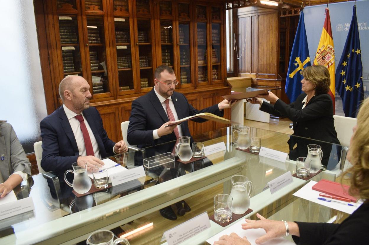 El presidente Adrián Barbón y la ministra Dolores Delgado se intercambian el convenio ante el vicepresidente Juan Cofiño. 