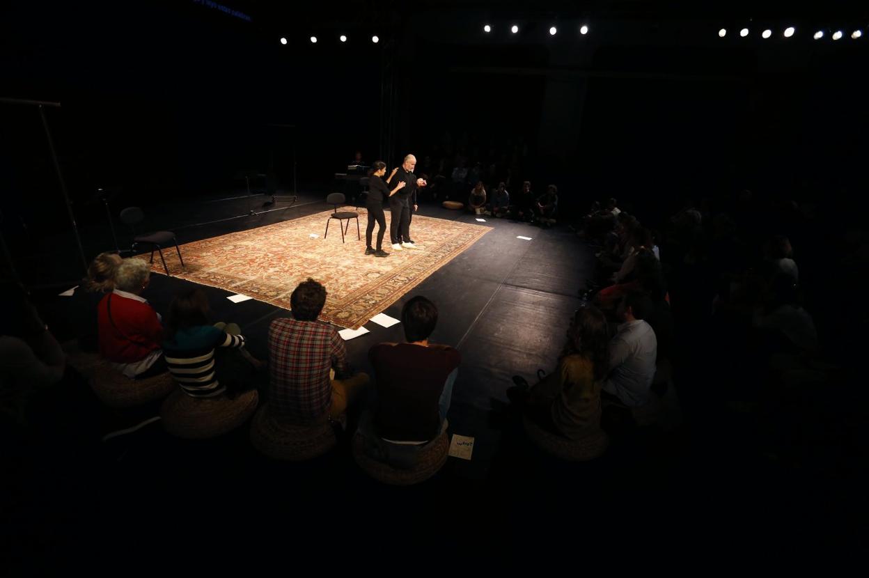 Los tres actores, rodeados del público, en un espacio solo decorado por una alfombra, sillas, atriles y percheros. :: FOTOS: PABLO LORENZANA