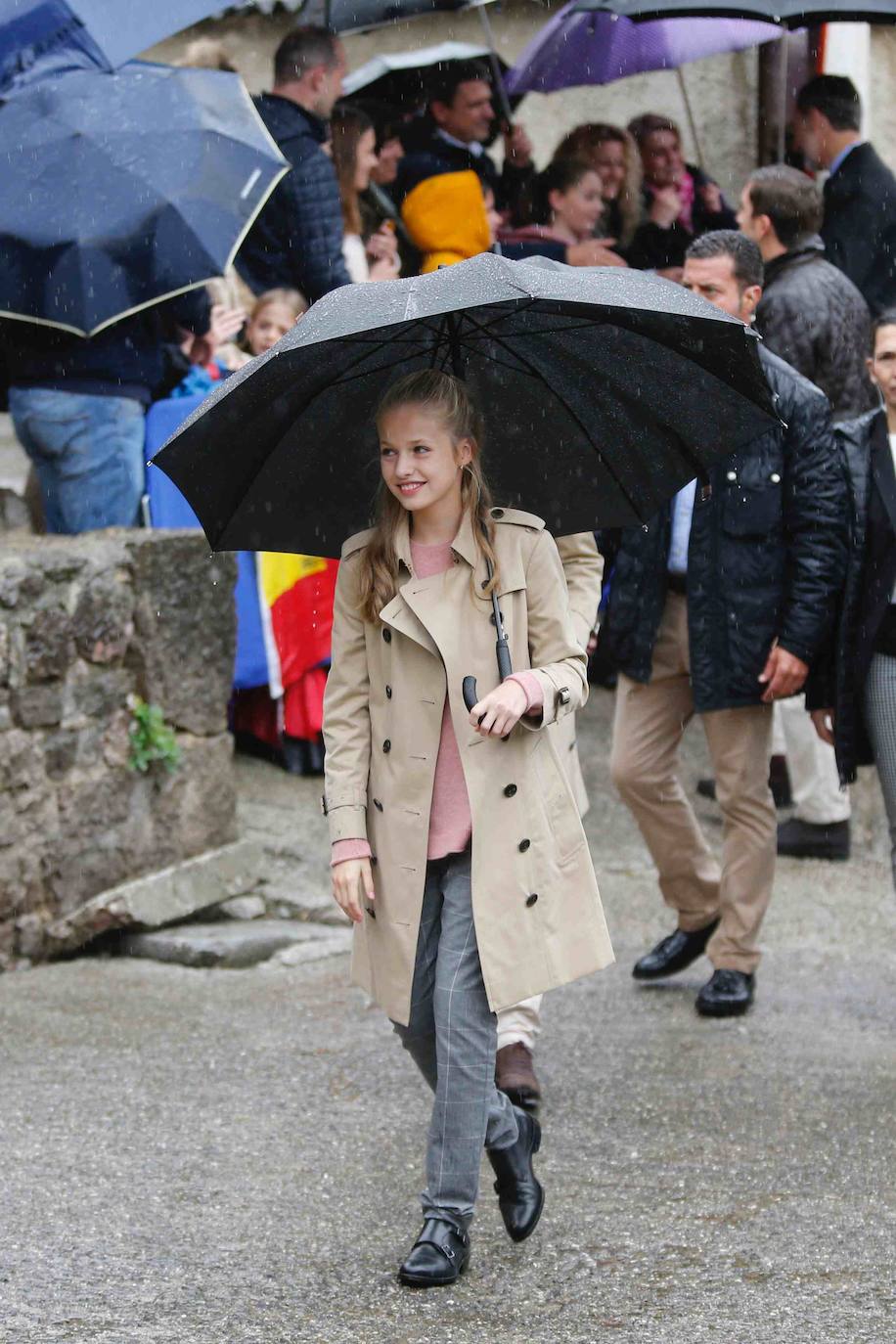 El look de la Princesa Leonor en Asiegu. Gabardina Burberrys decorte clásico con sueter rosay pantalón gris a cuadrospara el Pueblo Ejemplar. 