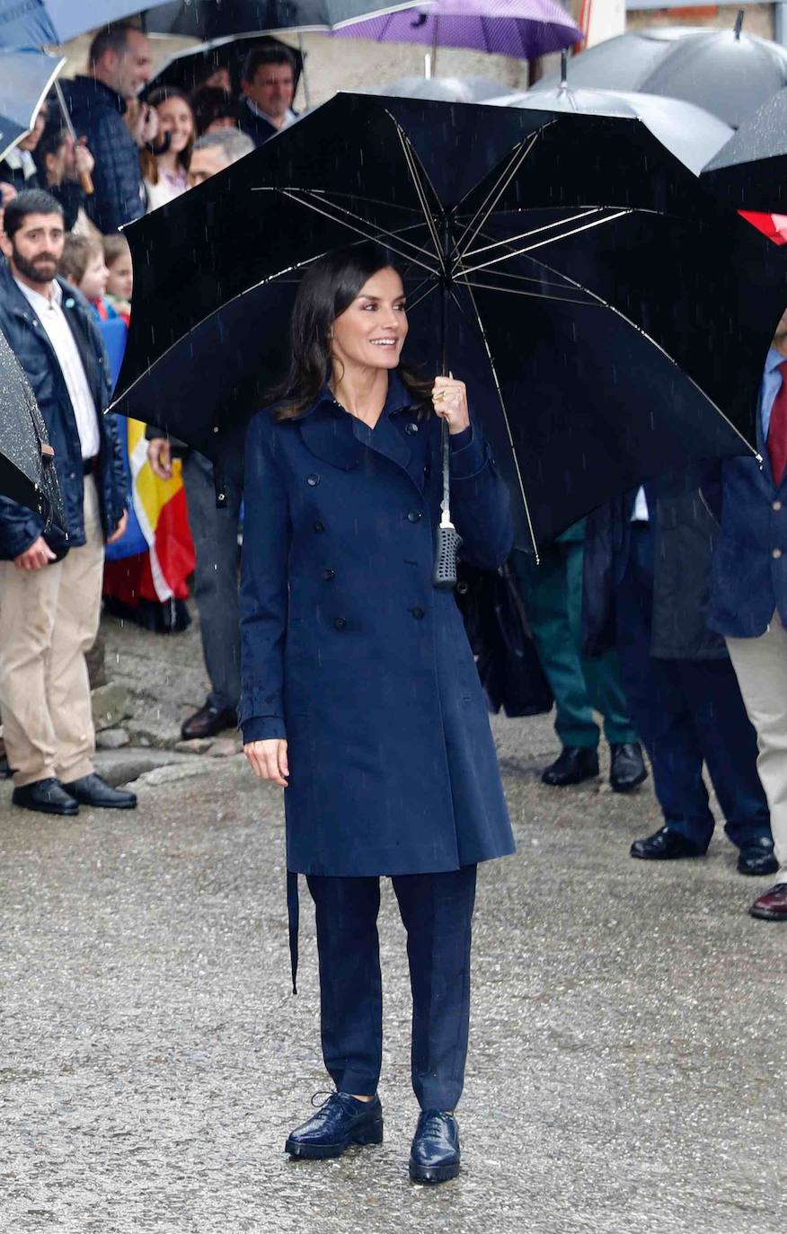 El look de la Reina Letizia en Asiegu. Gabardina azul y pantalones al tono, con zapatos de atar con suela de goma y paraguaspara el Pueblo Ejemplar. 