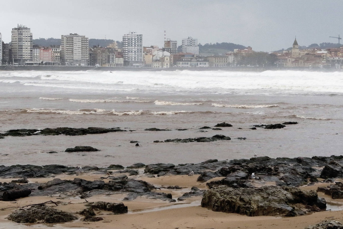 El temporal que azota Asturias ha ocasionado que la bahía de San Lorenzo apareciera este viernes con agua de color marrón, procedente del río Piles y del arrastre de las aguas de escorrentía, lo que se unió a una mar muy revuelta