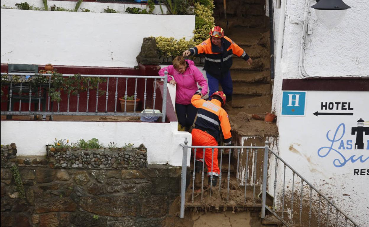 Voluntarios de Protección Civil ayudan a una de las afectadas a salir de su vivienda.