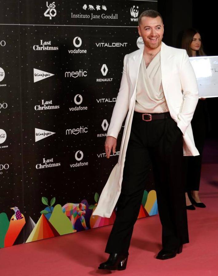 Sam Smith con esta opción mucho más arriesgada con pantalones de pinza negros acampanados, camisa de diseño drapeado y con escote en pico y chaqueta larga blanca tipo levita con cuello tipo solapa.