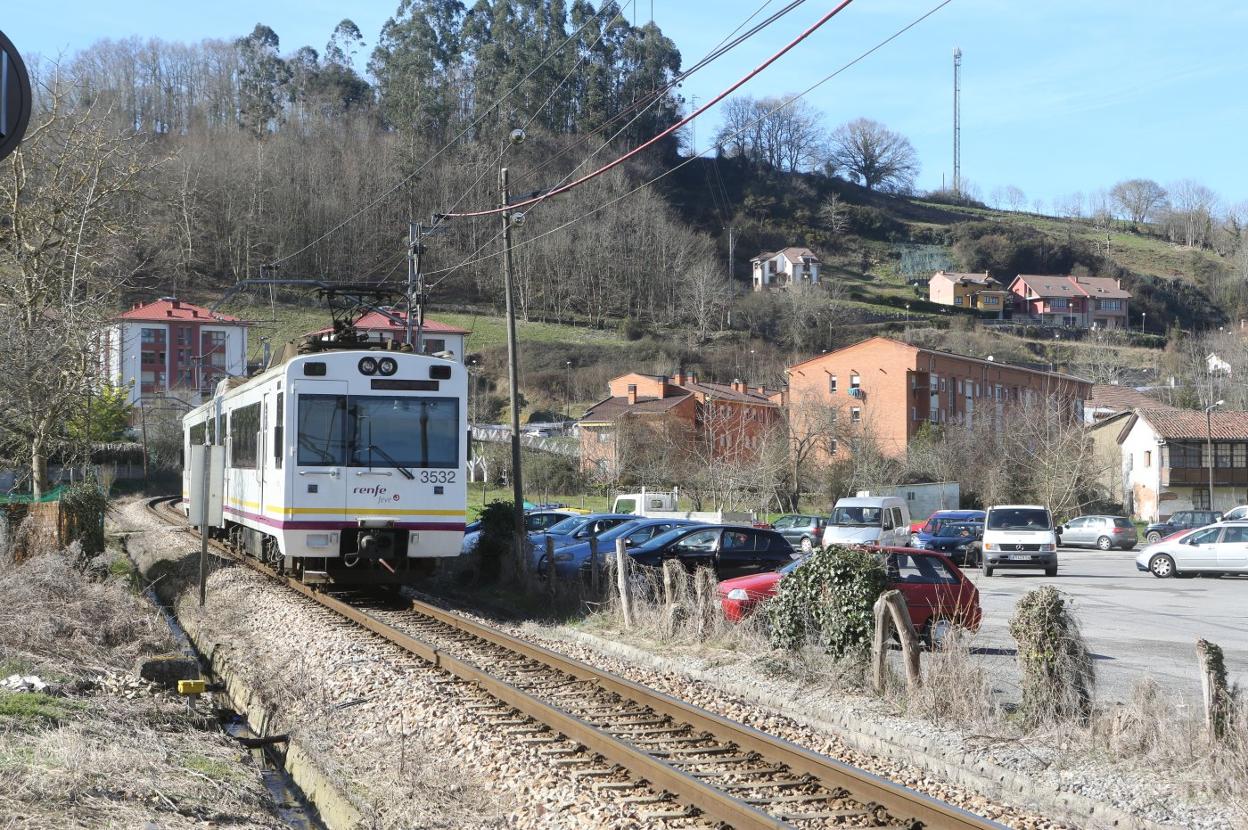 Un tren a su paso por la zona de Infiesto donde se suprimirá el paso a nivel, con el barrio de Xudes al fondo. 