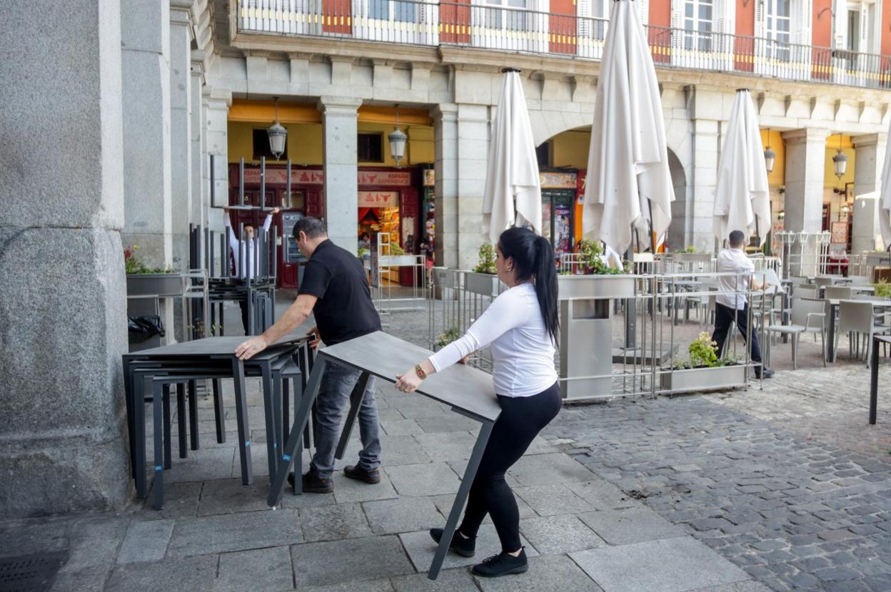 Varios empleados de un bar del centro de Madrid recogen la terraza del local. 