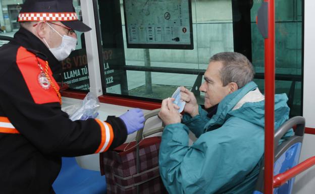 Un miembro de Protección Civil entrega una mascarilla a un usuario del transporte público en Gijón.