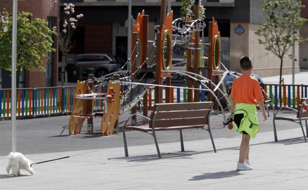 Un niño pasea a su perro junto a un parque infantil precintado. 