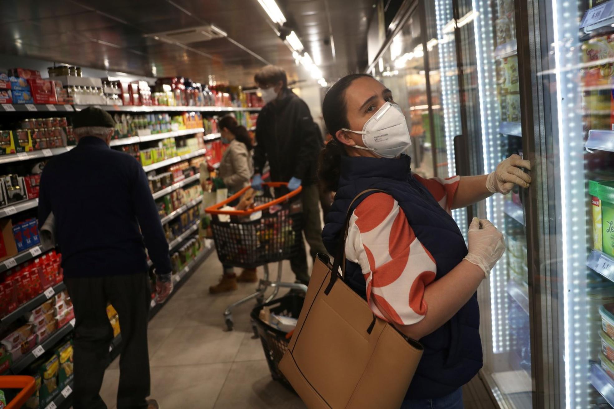 Varias personas hacen la compra en un supermercado, la mayoría usando mascarilla. 