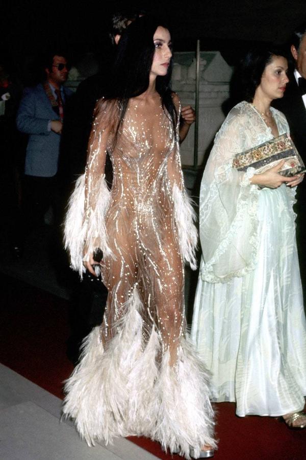 Mucho antes que Kendall Jenner o Kim Kardashian, ya existía una experta en defender los vestidos con transparencias (ahora conocidos como ‘naked dresses’) y no fue otra que Cher. La icónica cantante asistió a la gala MET en 1974 con un vestido de Bob Mackie de gasa, paillettes y plumas que pasó a formar parte de los archivos históricos de la moda y fue replicado en decenas de ocasiones por los grandes diseñadores. Sin ir más lejos, Kim Kardashian fue invitada a la gala MET de 2015 con un diseño de Peter Dundas para Roberto Cavalli que rendía homenaje al que llevó la artista californiana.