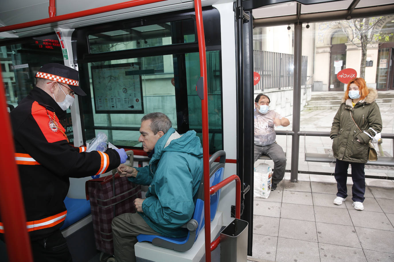 13 de abril. Gijón | Voluntarios de Protección Civil reparten mascarillas en las paradas de autobuses municipales de EMTUSA.