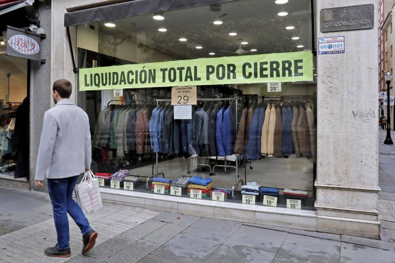 15 de mayo. Gijón | Un hombre pasea durante la fase 1 de la desescalada, cuando los pequeños negocios pueden volver a abrir. Al fondo se puede leer un cartel que pone «Liquidación total por cierre».