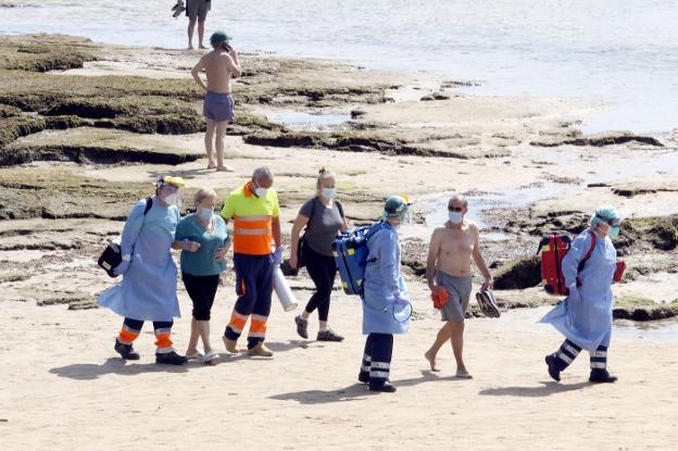 Sanitarios ayudan a salir del arenal de San Lorenzo a una mujer que sufrió ayer por la mañana una indisposición en la zona del pedrero de San Pedro. En el vídeo: El CTIC desarrolla una herramienta que permitirá controlar el aforo en las playas de Gijón.