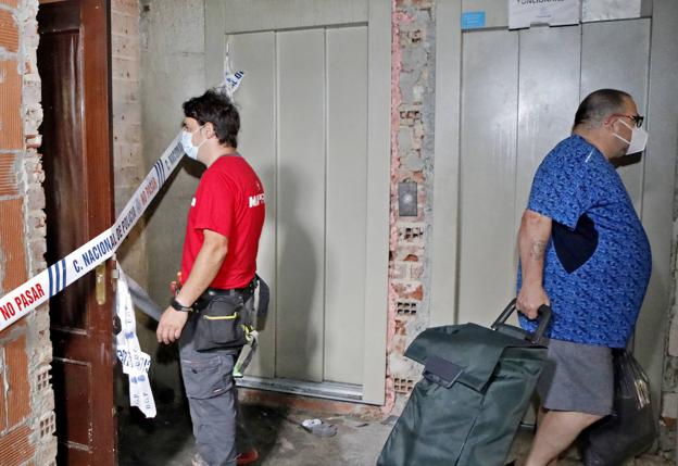 Un perito se cruza con un vecino con sus bolsas y maletas delante del ascensor en obras. 