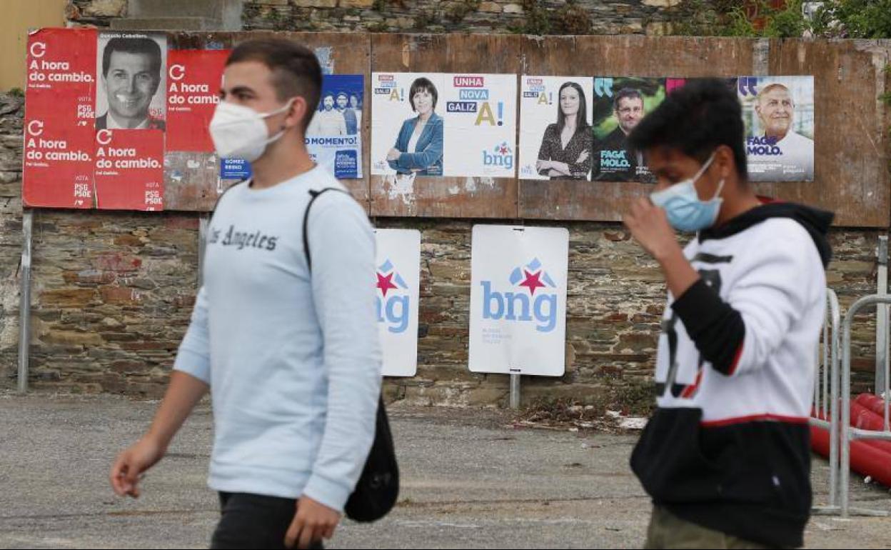 Dos jóvenes pasean en Foz (Lugo) por delante de unos carteles electorales.