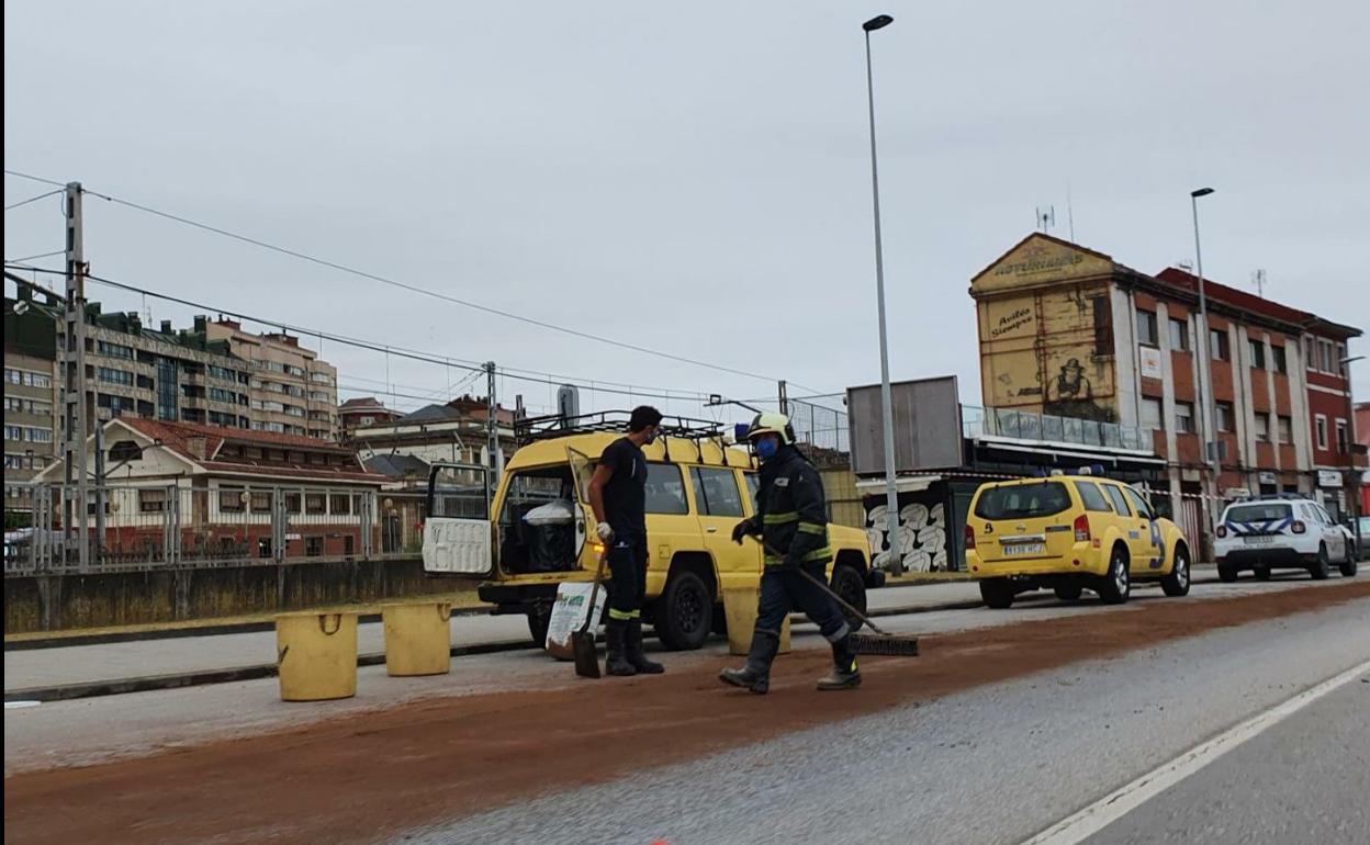 Dos bomberos cubren la calzada con material secante. 