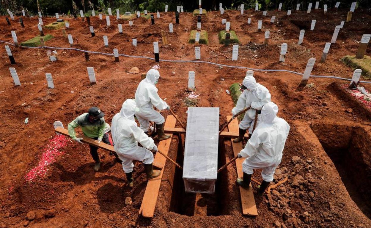 Varias personas con trajes aislantes entierran a una víctima de coronavirus durante su funeral celebra en el cementerio de Pondok Ranggon en Yakarta, Indonesia