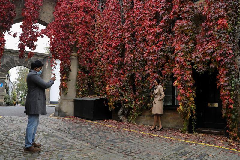 Una mujer posa para fotografías frente a hojas de otoño que cubren la fachada de una casa en Londres