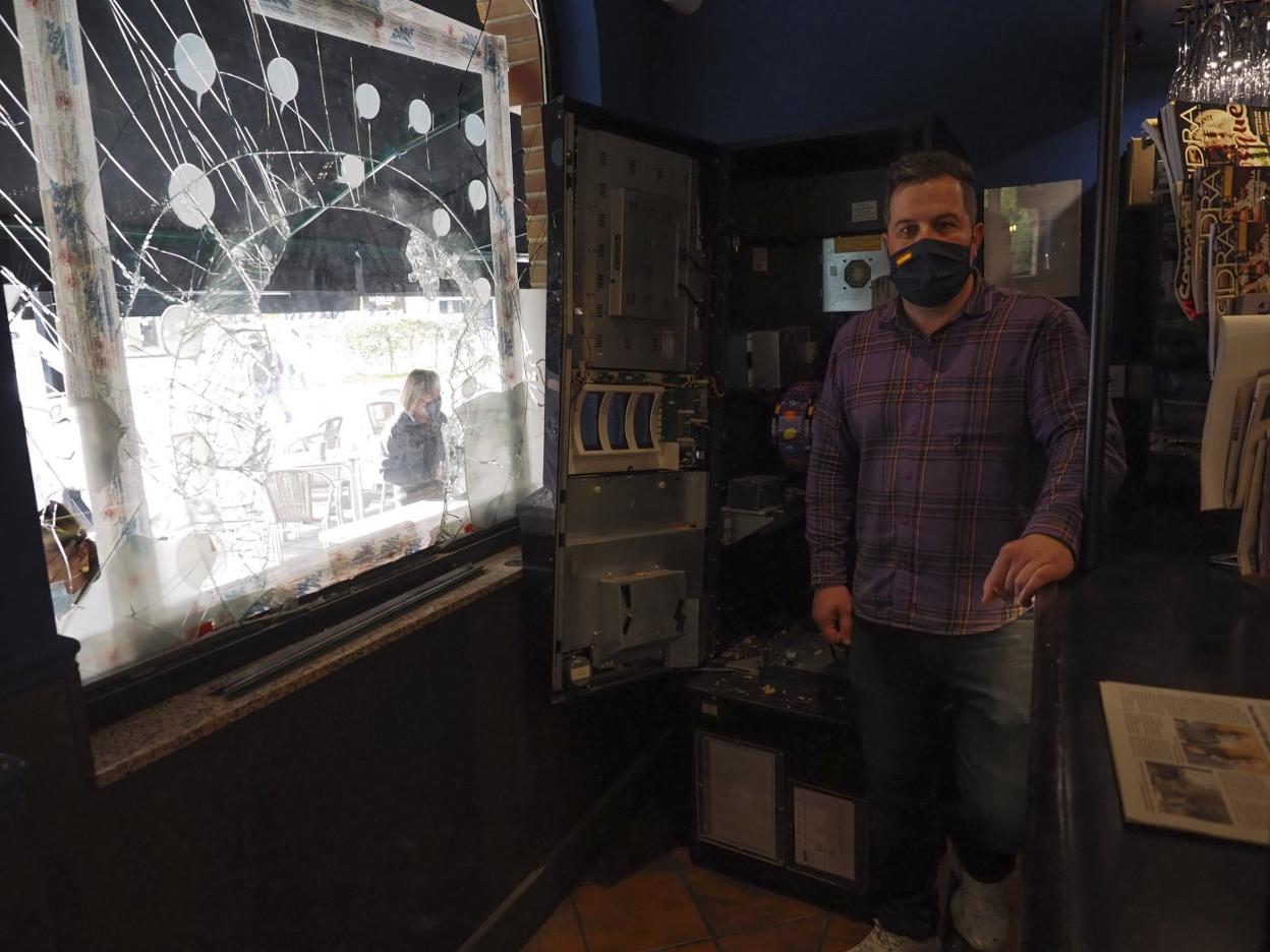 El propietario de La Tayuela, Roberto Valdés, ante el cristal roto del negocio y con la máquina tragaperras al fondo. 