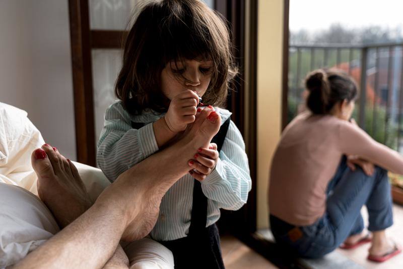 Marzio Toniolo, un profesor de 35 años, toma una foto de su hija Bianca de dos años pintándole las uñas de los pies mientras su esposa, Chiara Zuddas, mira desde el balcón de su casa durante la pandemia del coronavirus, en San Fiorano, Italia, 20 de marzo de 2020. 