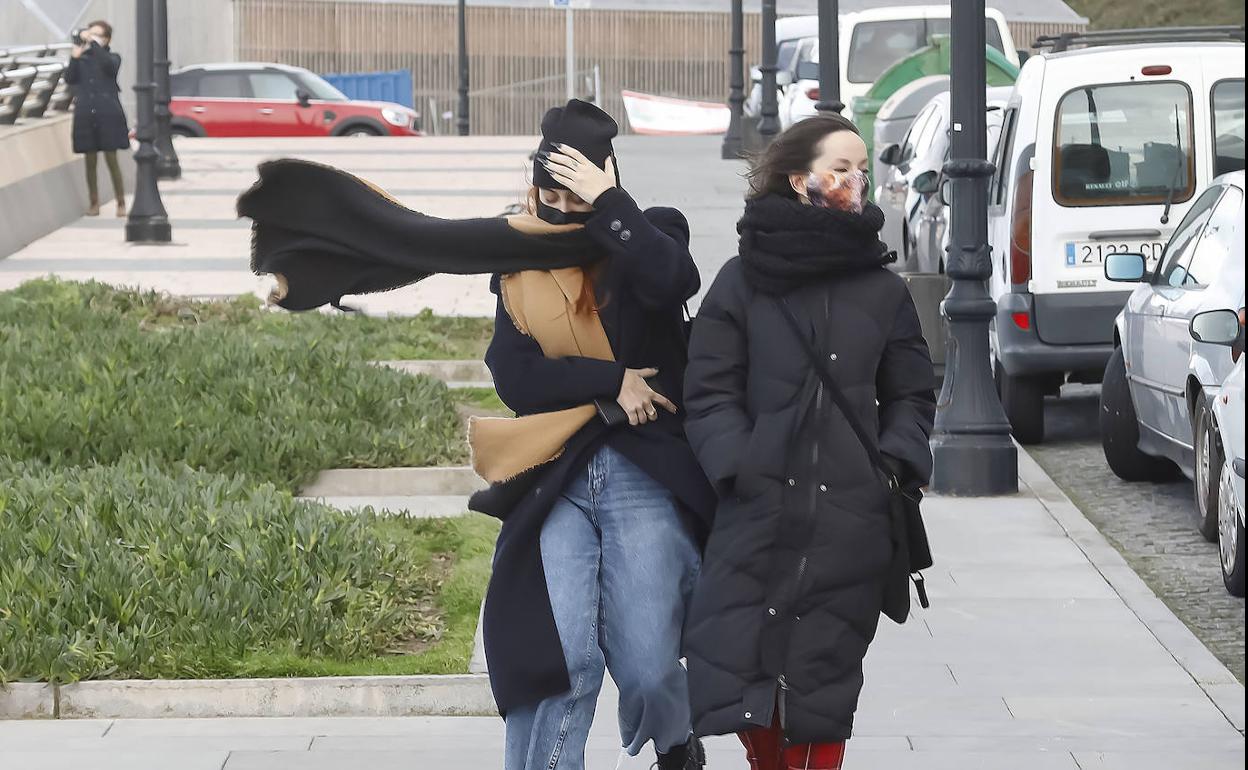 Dos mujeres transitan por una calle de Gijón en una jornada de fuertes vientos.