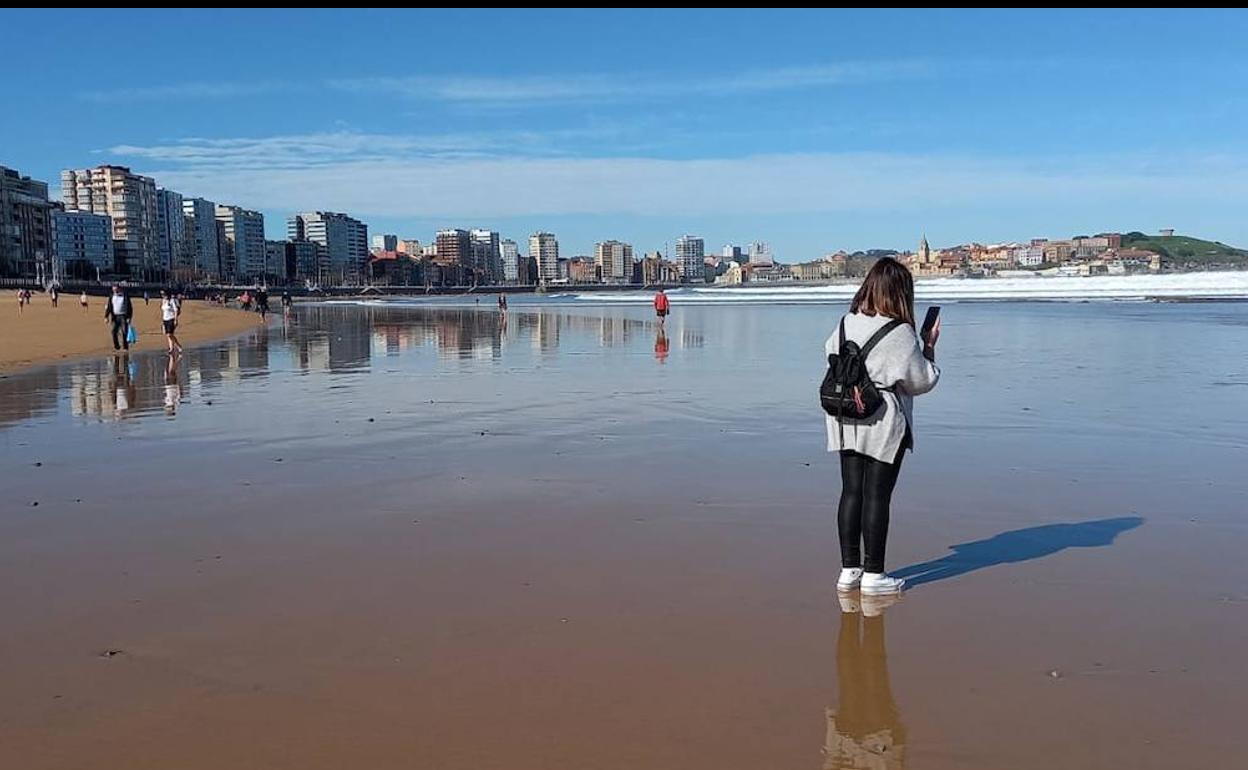 Una joven mira su movil este miércoles en la playa de San Lorenzo de Gijón, donde han ido a disfrutar del buen tiempo decenas de gijoneses. 