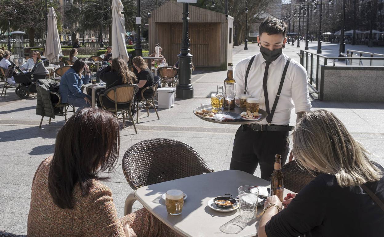 Un camarero atiende a dos clientas en una terraza de Gijón 