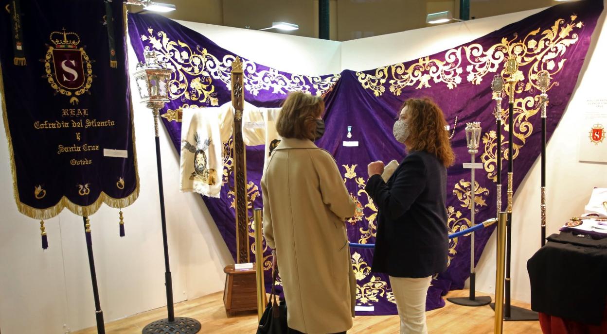 Dos asistentes a la inauguración, frente a uno de los mantos y estandartes expuestos. 