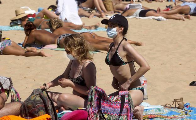 Dos mujeres toman el sol con mascarilla en la playa del Sardinero, en Santander.