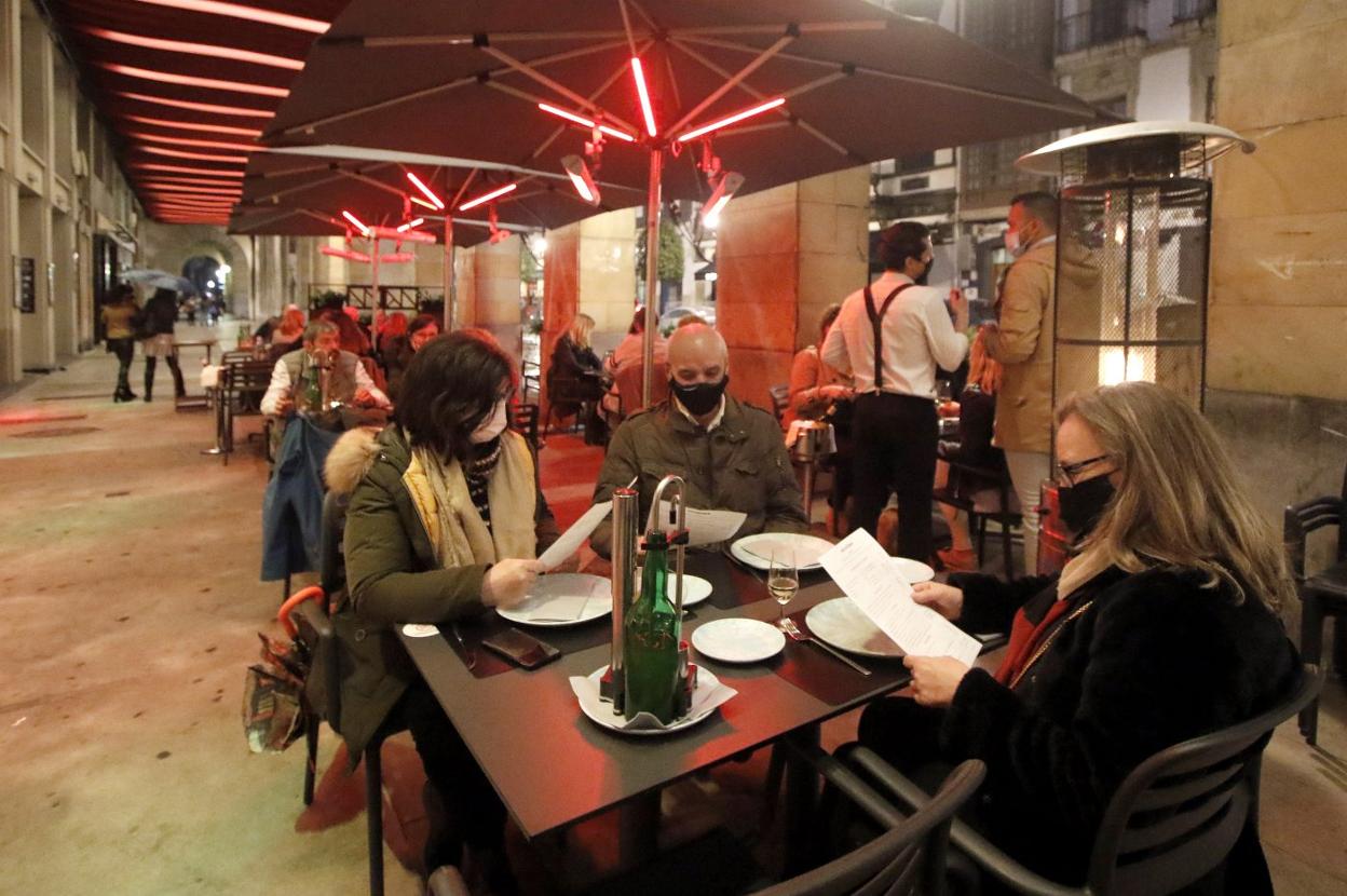 Varias personas miran la carta de un restaurante en una terraza en los soportales de Marqués de San Esteban, en Gijón. 