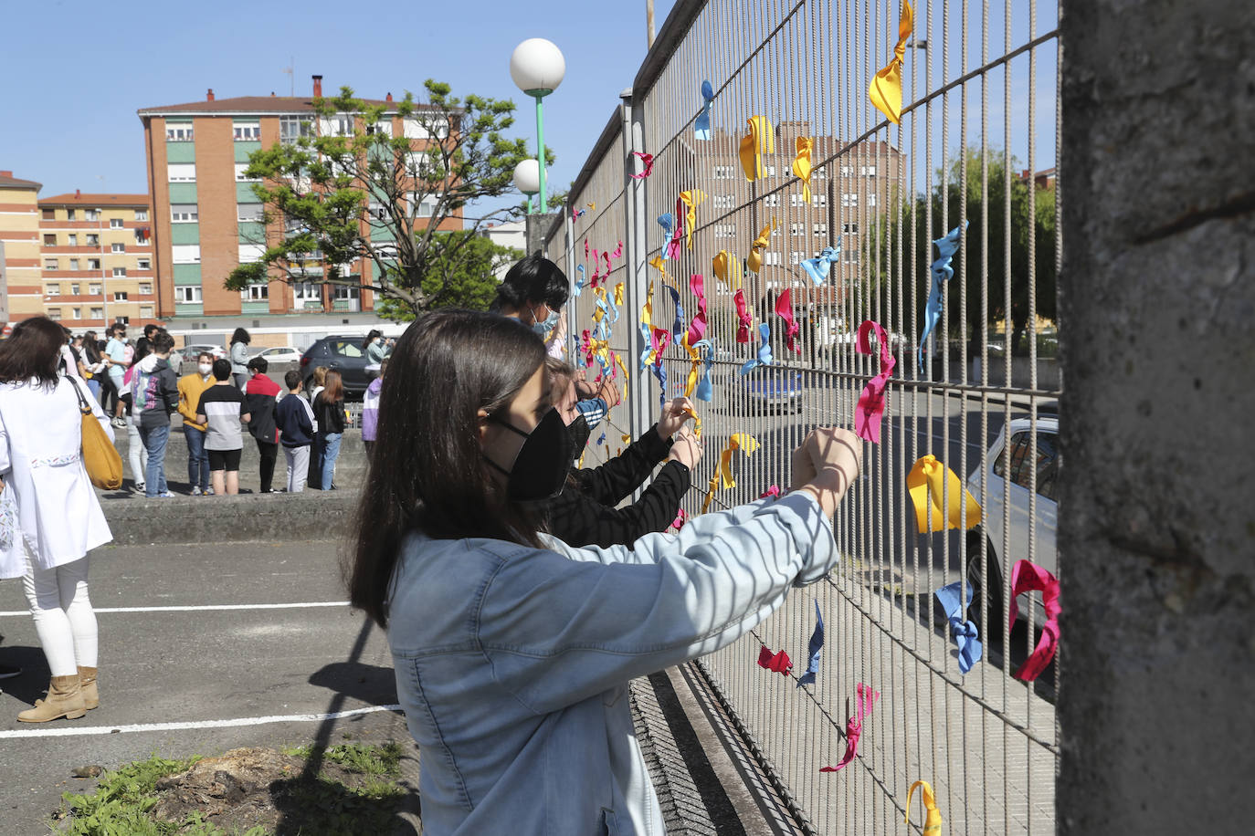 Un total de 150 alumnos han salido de sus clases para realizar un acto en el que los escolares han colocado lazos de colores, que contienen deseos formulados con la ilusión de un viaje, en la valla frontal del patio para formar una cadena de deseos entrelazados.