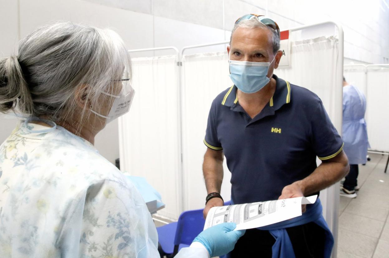 Un ciudadano recibe un folleto informativo sobre posibles reacciones a la vacuna tras recibir una dosis en el Palacio de Deportes de Gijón. 