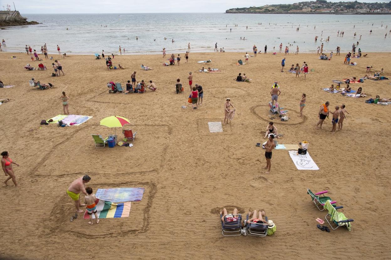 Gijón. Usuarios de la playa, delimitando la zona donde están instalados para guardar la distancia de seguridad. 
